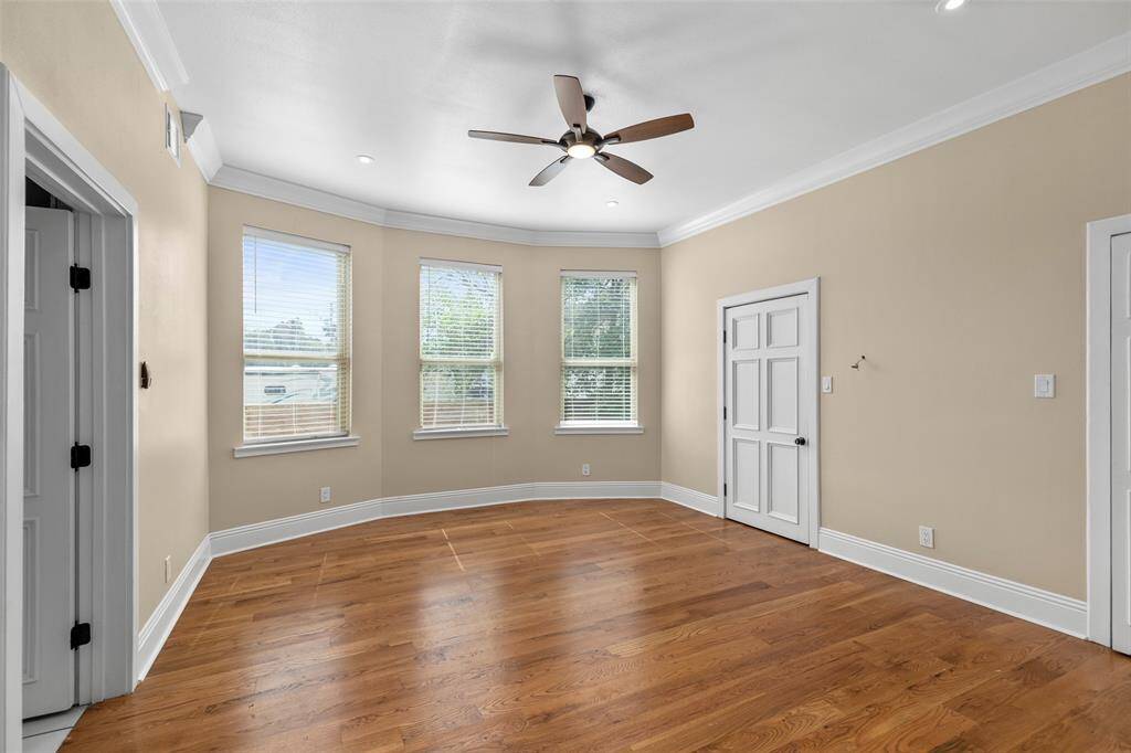 This is a spacious, well-lit primary bedroom with hardwood flooring features multiple windows allowing for natural light.
