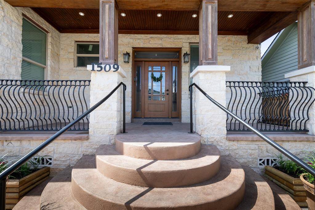 Charming entrance featuring a stone facade, elegant wooden door, and decorative iron railing, complemented by a welcoming semi-circular staircase.