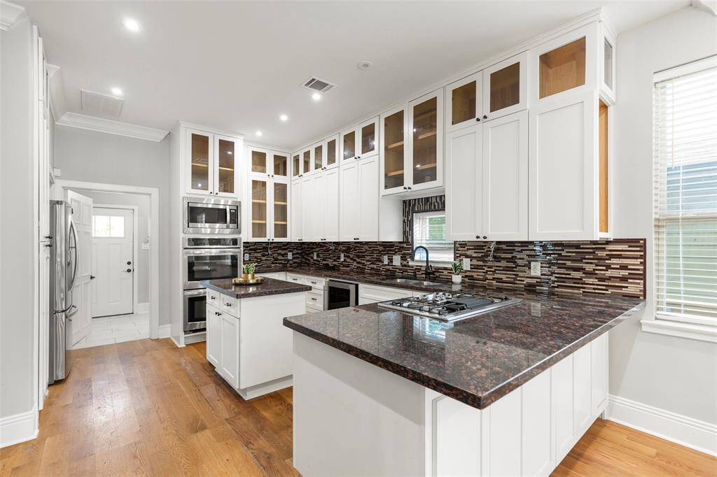 1509 Summer St offers a modern kitchen with white cabinetry, granite countertops, a gas cooktop, built-in stainless steel appliances, a tiled backsplash, hardwood floors, and recessed lighting.