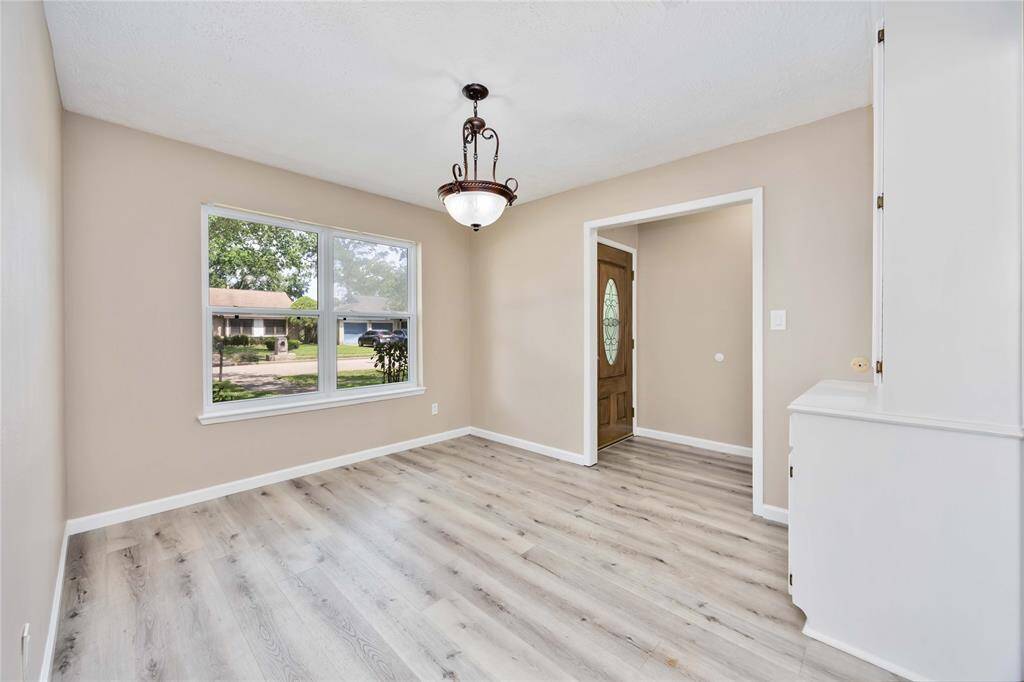 Bright, inviting entryway with light wood flooring, neutral walls, and a stylish chandelier. Large window offers natural light and a view of the front yard.