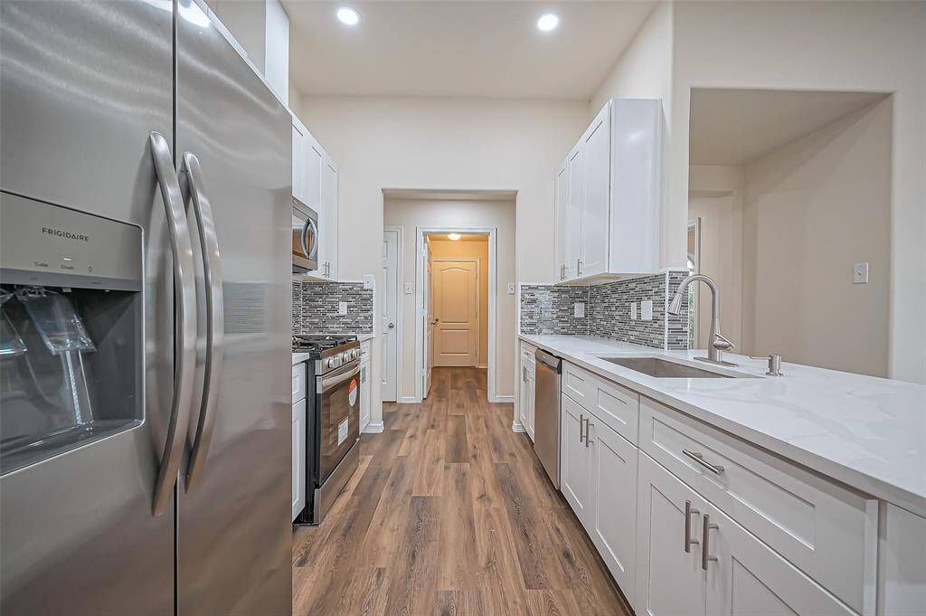 The kitchen features a French-style side-by-side, stainless steel Frigidaire refrigerator with ice and water in the door for added convenience. An open door at the far end leads to the utility room and attached 2-car garage. To the left, you'll find a pantry, providing ample storage space for all your essentials.