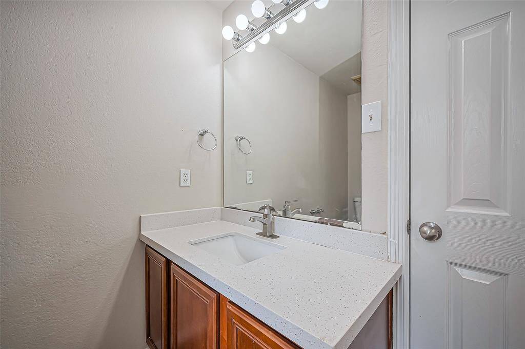 The left-hand sink vanity features a sleek quartz countertop with an undermount sink, complemented by an updated faucet. A wall mirror enhances the space, while overhead Hollywood lighting provides bright, stylish illumination.