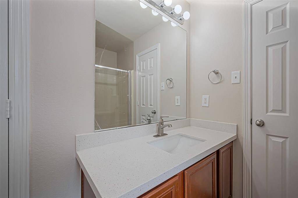 The right-hand sink vanity mirrors the left, featuring a sleek quartz countertop with an undermount sink, an updated faucet, and a wall mirror. Overhead Hollywood lighting adds bright, stylish illumination, creating a cohesive and well-lit space.