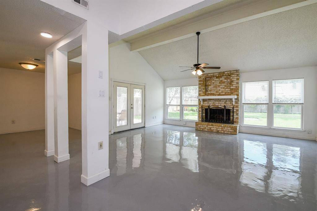 This spacious living area features high ceilings, a brick fireplace, and large windows providing plenty of natural light. The floors are sleek and polished, and there's access to the backyard through French doors. Ideal for entertaining and relaxation.