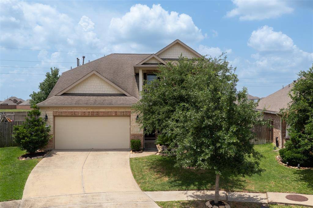 The front yard is landscaped with lush greenery and a palm plant, and the exterior showcases a combination of stone and brick with a welcoming entrance pathway.