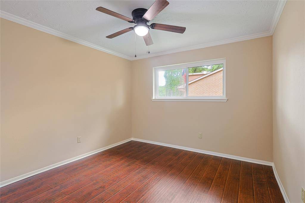 This room features warm-toned walls, rich wood flooring, and a ceiling fan with overhead lighting. A window provides natural light, offering a cozy and inviting space.