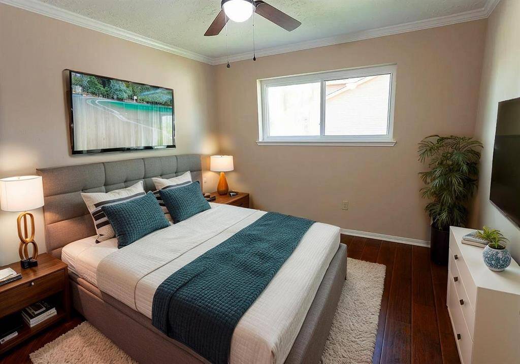 This cozy bedroom features  warm wooden floors, a ceiling fan, and ample natural light from the window, creating a comfortable and inviting atmosphere.