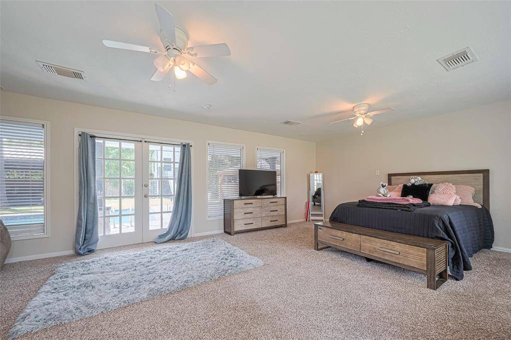 Spacious bedroom with french doors open to a view of the pool, adding natural light.