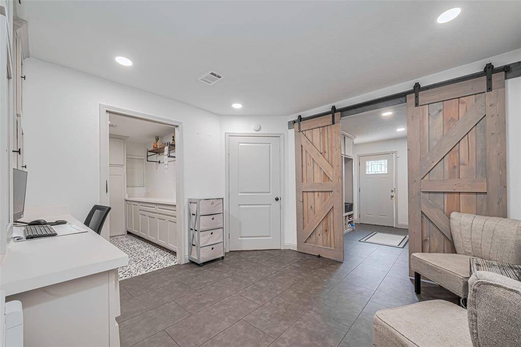 This space flows from the mudroom and features an entryway with stylish barn doors and recessed lighting. There's a small office nook on the left with built-in cabinetry and a view into a tiled laundry room.