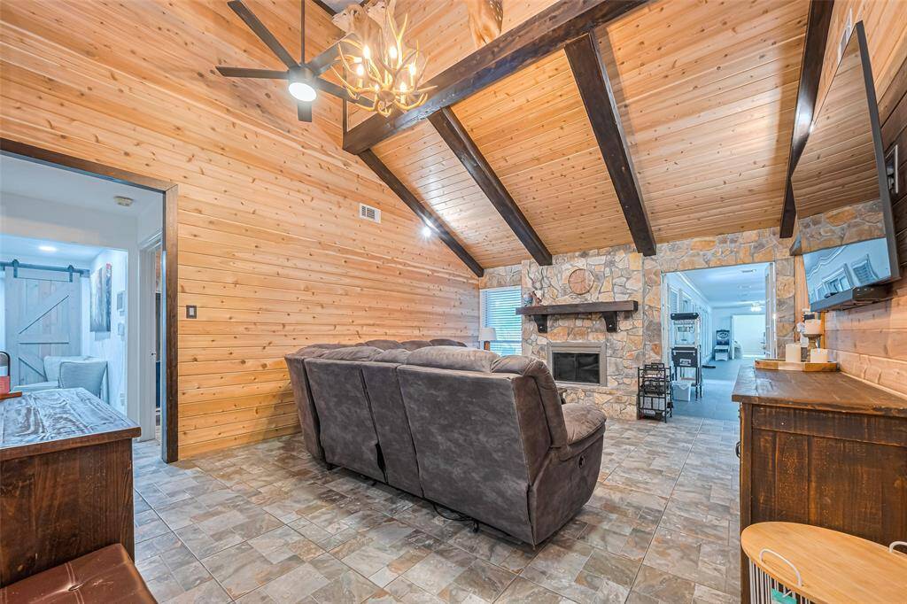 This cozy living room features a rustic design with wood-paneled walls and ceiling, exposed beams, and a stone fireplace.