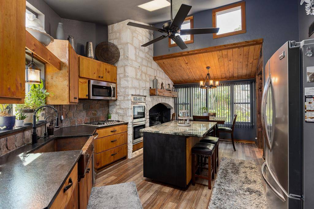 Gourmet kitchen features skylight, vaulted ceiling, stainless steel appliances, double oven, commercial grade gas range, custom-built knotty pine wood cabinets with 42" uppers, onyx leather granite countertops, under-mount hammered copper sink & a slate backsplash.