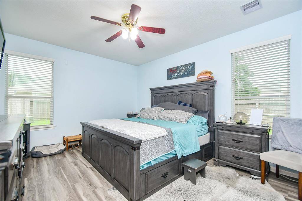 This cozy bedroom features light blue walls, a ceiling fan, and ample natural light from two large windows