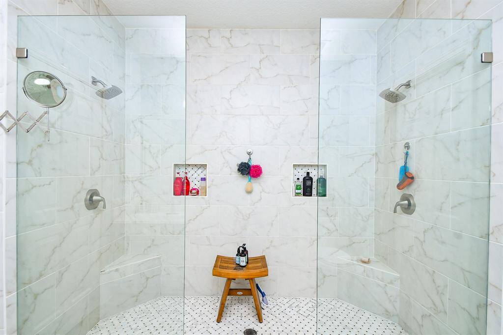 Glass-enclosed shower is tiled throughout and the flooring is marble. Note the two shower heads!