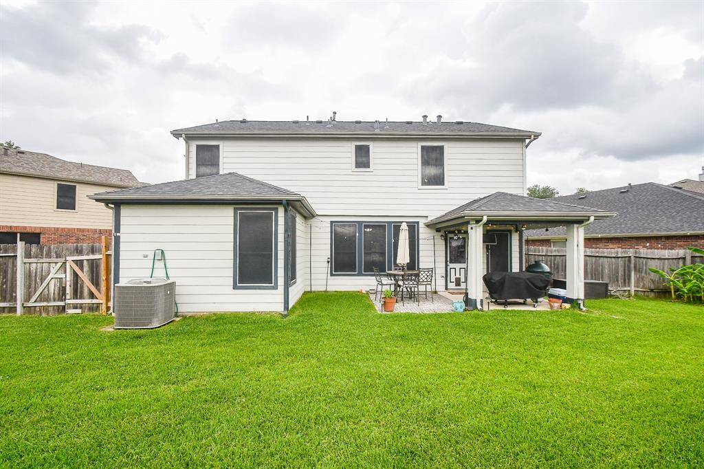 The backyard features a well-maintained lawn, a small patio area with outdoor seating, and a covered space with a grill. The yard is enclosed by a wooden fence, providing privacy