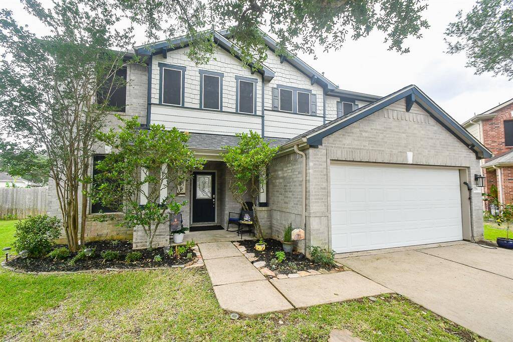 This charming two-story home features a gray brick exterior with white accents, a neatly landscaped front yard, a cozy porch, and a spacious two-car garage.
