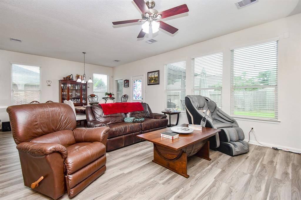 A spacious, well-lit living area with large windows,  The open layout flows into breakfast area, highlighted by elegant light fixtures and a view of the backyard.