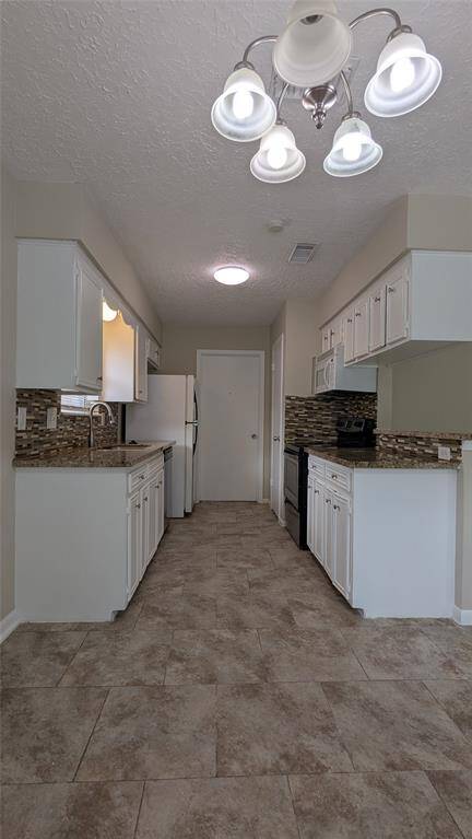 This kitchen features a galley layout with white cabinetry, a tiled floor, and a modern light fixture. It includes a tiled backsplash and standard appliances, providing a functional cooking space.