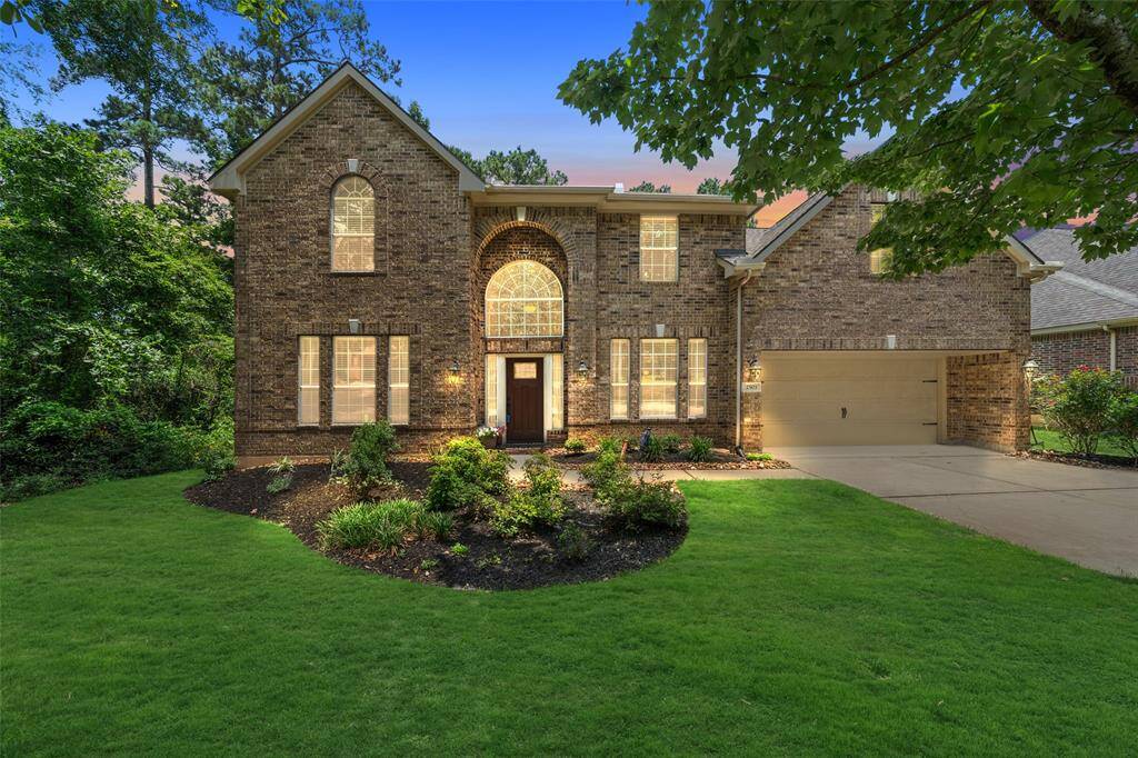 This photo showcases a stately two-story brick home with an elegant arched entryway and large windows. The well-maintained front yard features lush landscaping, and the property includes a spacious driveway leading to an attached garage. Perfect for a family seeking a welcoming and stylish residence.