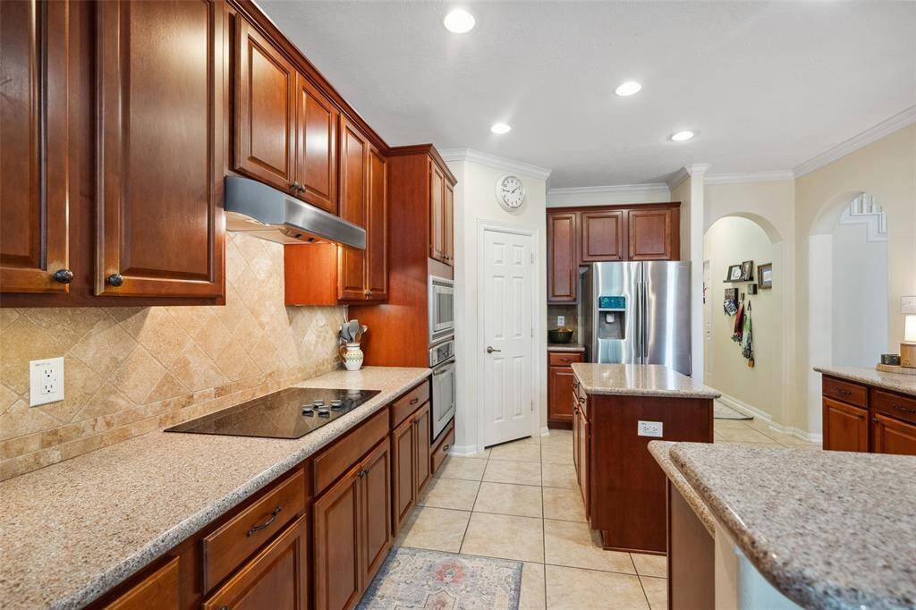 Built-in oven, cooktop, and a central island, all illuminated by recessed lighting. The neutral tile flooring complements the warm on trend tones, creating an inviting atmosphere.