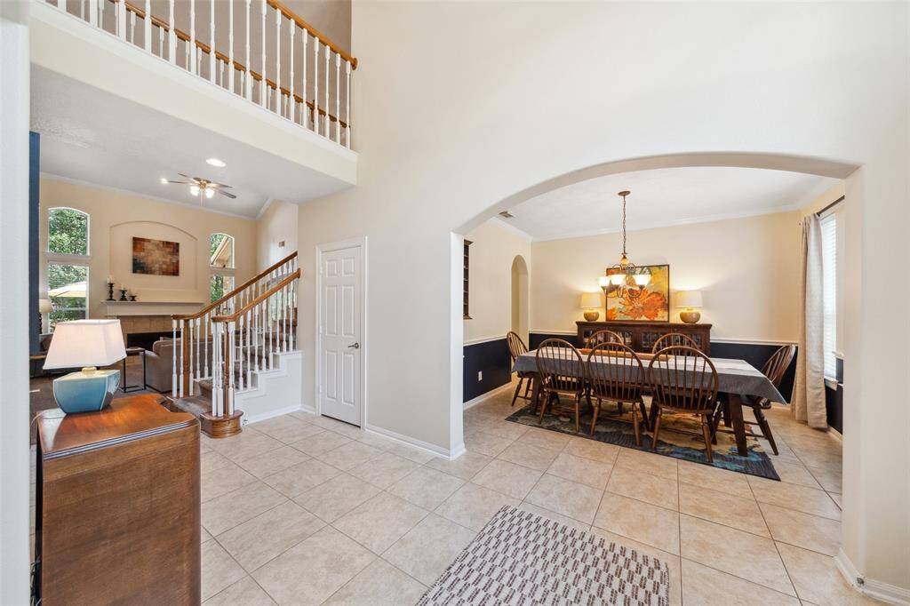 This inviting home features a spacious, open-plan layout with a tiled entryway leading to a bright living room with high ceilings and a cozy fireplace. Adjacent is a formal dining area with elegant lighting, perfect for entertaining. The staircase and large windows enhance the airy feel, creating a warm and welcoming atmosphere.