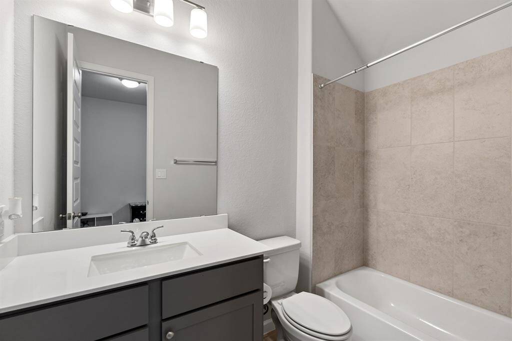 This beautiful bathroom features a tiled shower/tub combo, a stylish brown vanity with a sleek quartz countertop, and a modern toilet, offering both elegance and functionality!