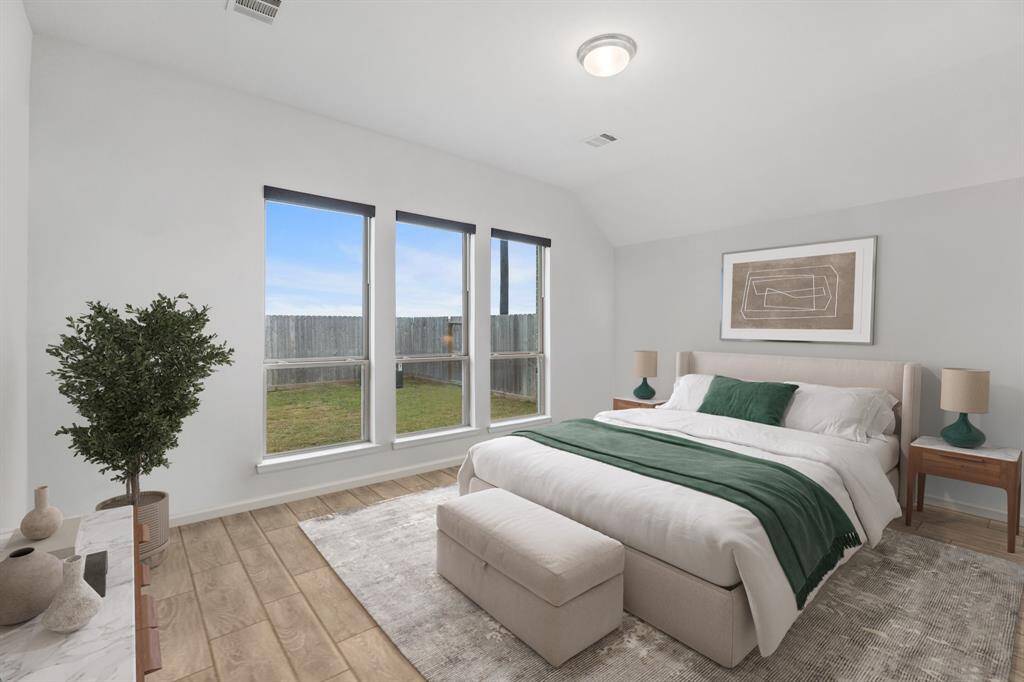 This spacious primary bedroom boasts multiple windows with roller shades, elegant wood-look tile flooring, and soaring vaulted ceilings, creating a bright and inviting retreat! *Virtually Staged*