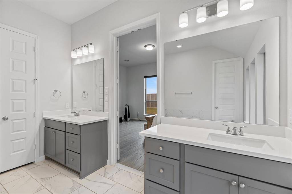 The primary bathroom features stylish double grey sink vanities and sleek tile flooring, offering both function and modern elegance!
