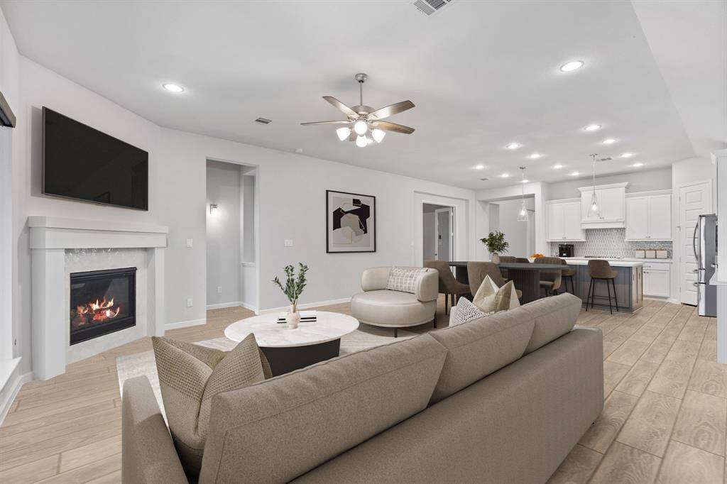 This inviting living room features a stylish white gas fireplace, elegant wood-look tile flooring, recessed lighting, and large windows with sleek roller shades, creating a bright and cozy atmosphere! *Virtually Staged*