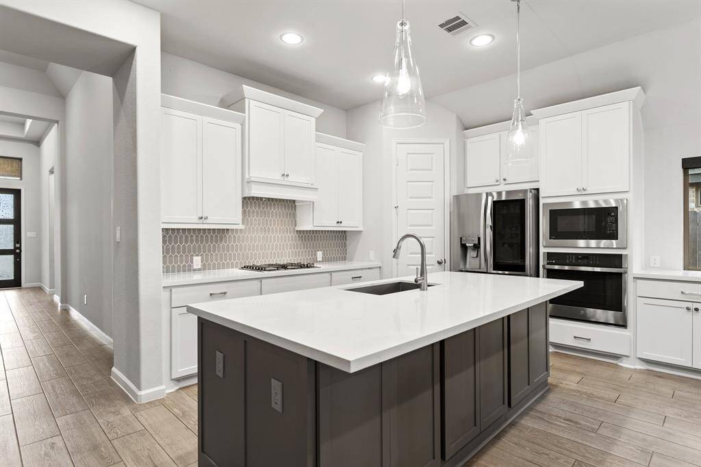 Experience a chef's dream in this kitchen, featuring crisp white cabinets, a large kitchen island, a built-in microwave/oven, and striking modern pendant lighting for both style and functionality.