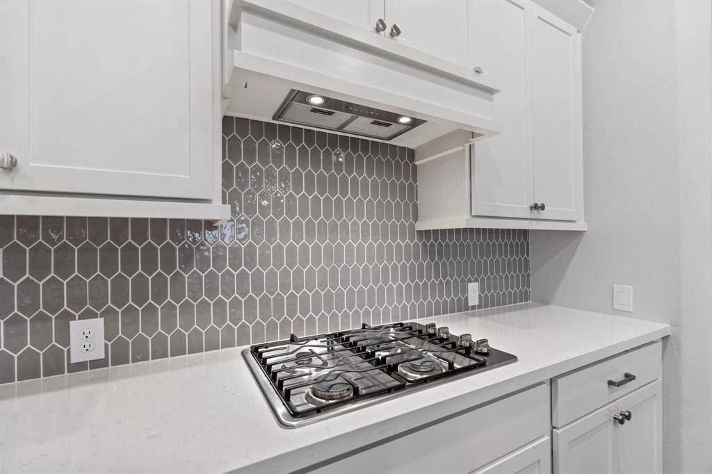 Enjoy this stunning close-up of the custom grey backsplash, sleek modern white vent, and high-end gas stovetop, adding both style and functionality to your kitchen!