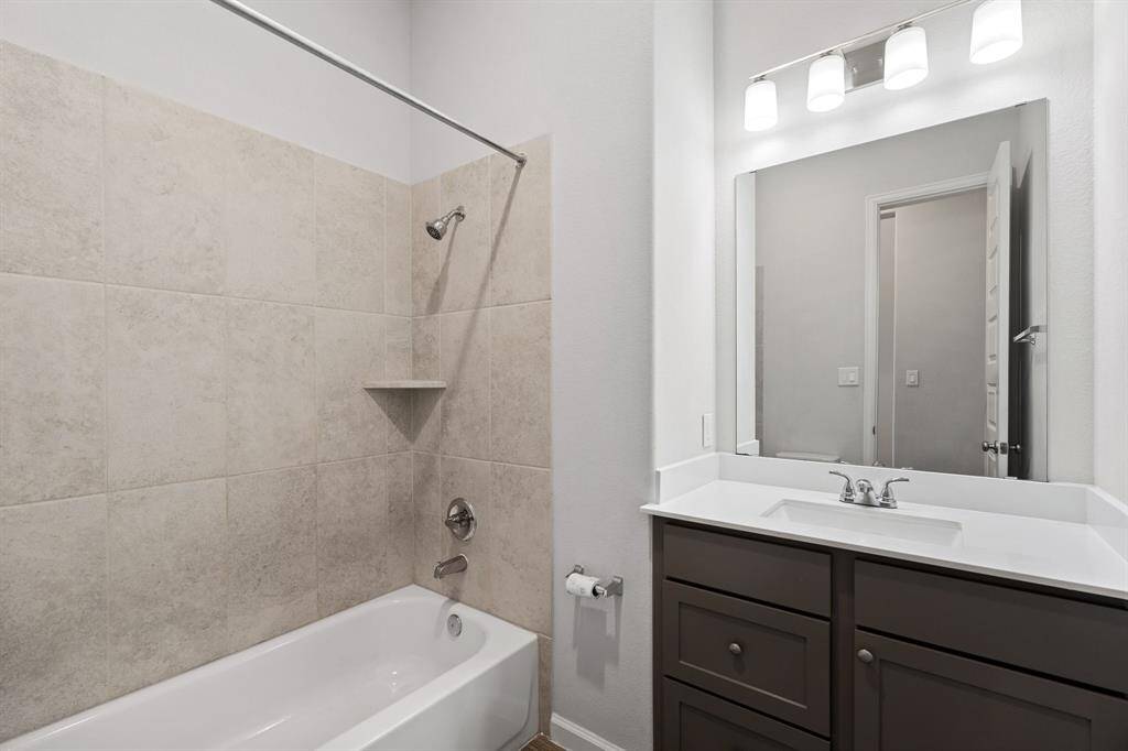 This beautiful bathroom features a tiled shower/tub combo, a stylish brown vanity with a sleek quartz countertop, and a modern toilet, offering both elegance and functionality!