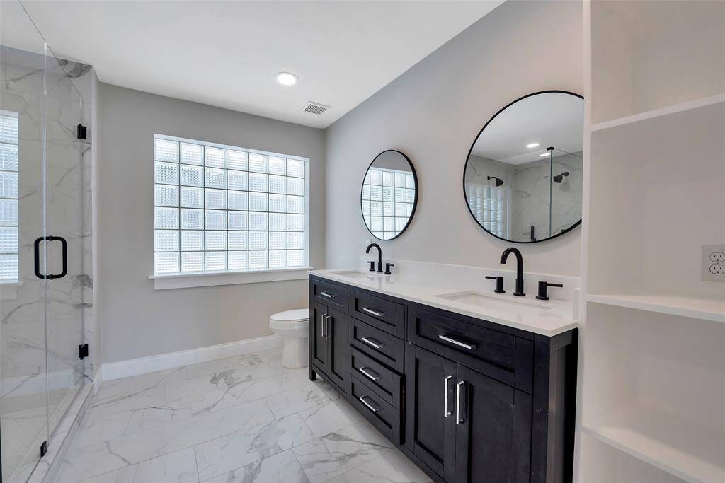 Primary bathroom with a spa-like atmosphere. Glass block privacy window and updated vanity with dual sinks and circle mirrors give a modern feel!