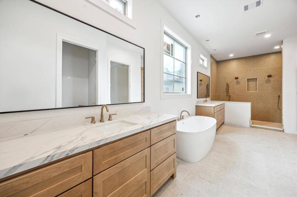 Exquisite Primary Bath includes abundant storage with elegant pendant lights, oversized mirrors, soaking tub, and glass-encased shower. Large window allows for natural light in this relaxing suite.