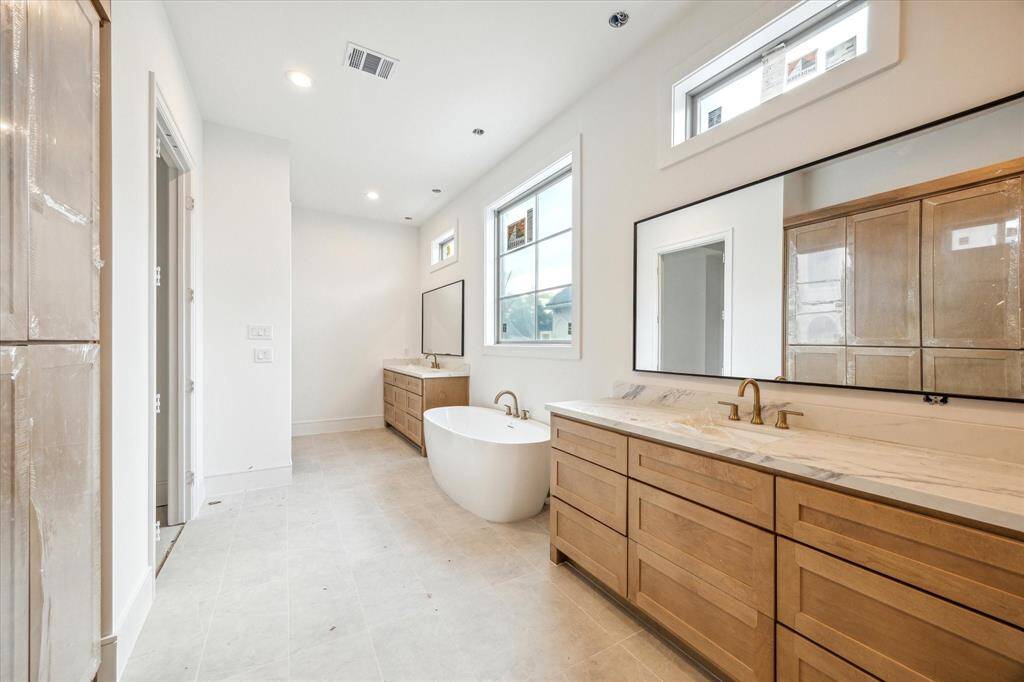 Two vanities with Quartz countertops, abundant storage, and additional counter space flank an oval soaking tub.