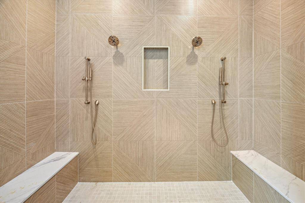 Glass-encased shower with mosaic tile floors, custom niche, dual heads and built-in seat in the Primary Bathroom.