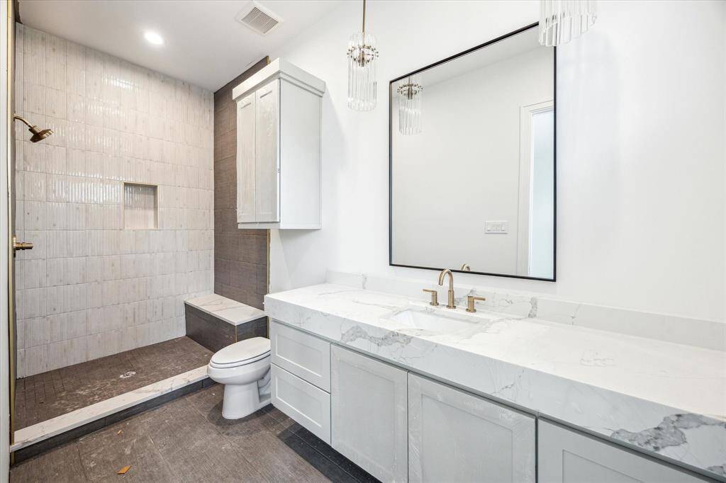 En-suite bathroom for second-floor bedroom includes a glass-encased shower with fluted tiles along the shower wall and niche. Quartz countertops, floating shelves, and hanging pendent lights complete this bathroom.