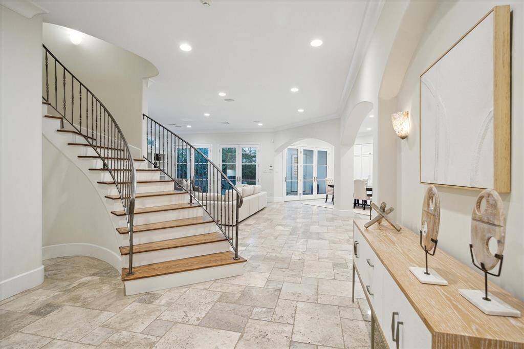 This elegant foyer features a graceful, curved staircase with wrought iron railings, leading to an open and spacious living area.