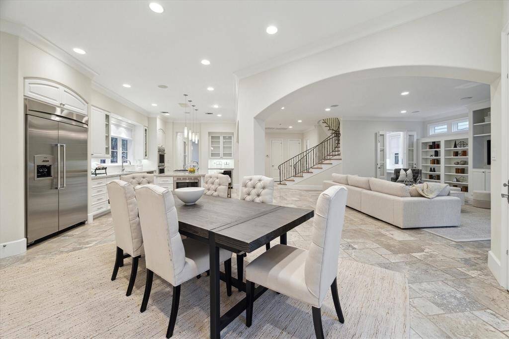 This open-concept living area features a modern kitchen with stainless steel appliances, a spacious dining area, and a cozy living room. The neutral palette and recessed lighting create a bright, inviting atmosphere. A stylish staircase leads to the upper floor, complemented by built-in shelving for added storage.