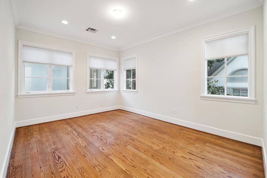 Bright secondary bedroom with hardwood floors and neutral walls, featuring three large windows.