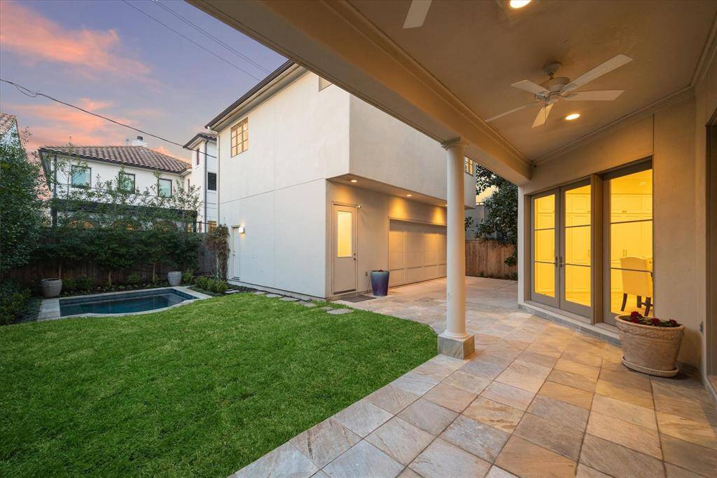 The lush backyard featuring a covered patio elegant tile flooring, and French doors. The well-maintained lawn leads to a small pool, surrounded by lush landscaping, providing a serene outdoor setting.