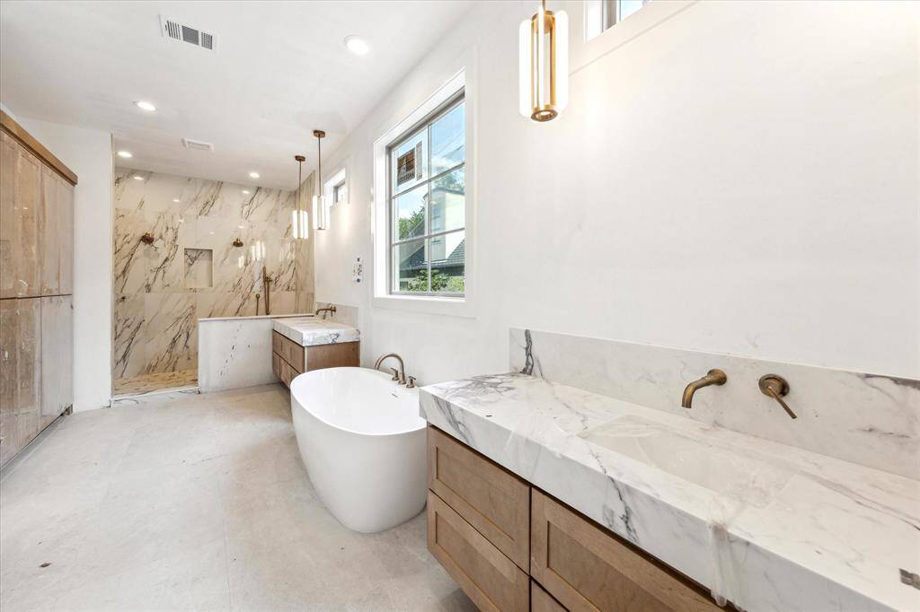 Exquisite Primary Bath features sun bleached floating shelves with elegant pendant lights, oversized mirrors, soaking tub, and glass-encased shower. Large window allows for natural light in this relaxing suite.