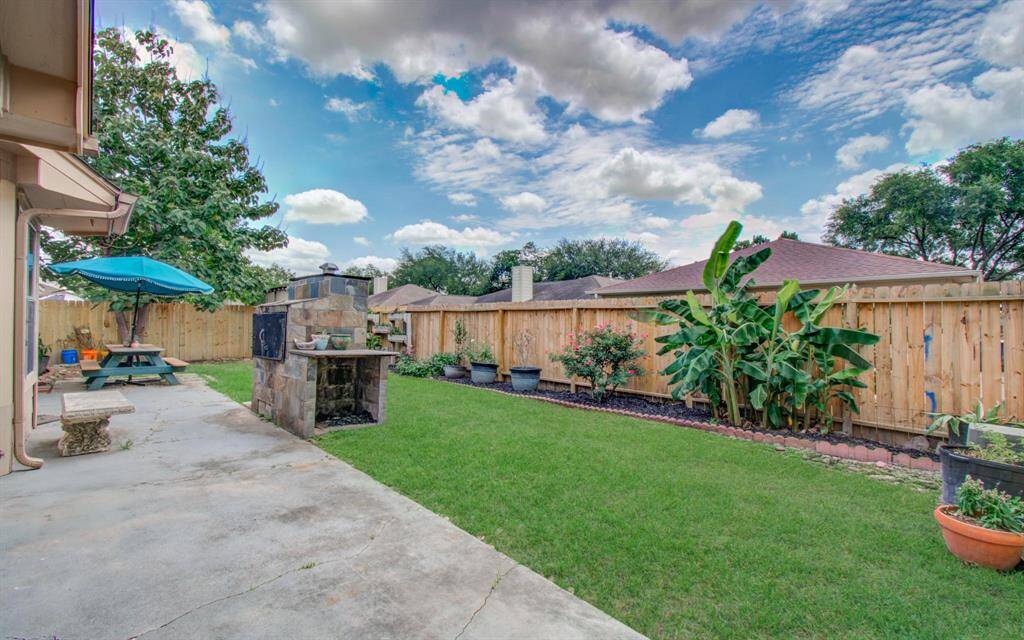 Outdoor living zone – Stone grill/smoker anchors an extended patio overlooking banana trees, rose bushes and a fresh privacy fence. (virtually staged)