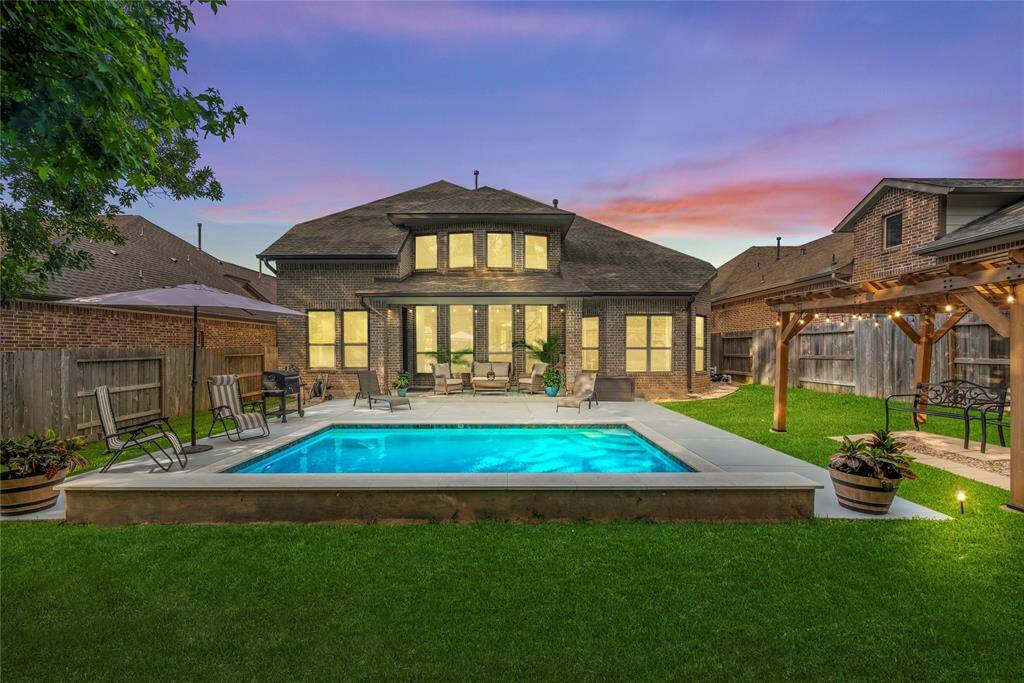 Backyard Oasis: Enjoy resort-style living in your own backyard, featuring a sparkling pool, expansive patio, custom pergola, lush green lawn, and beautiful sunset views—perfect for entertaining or relaxing.