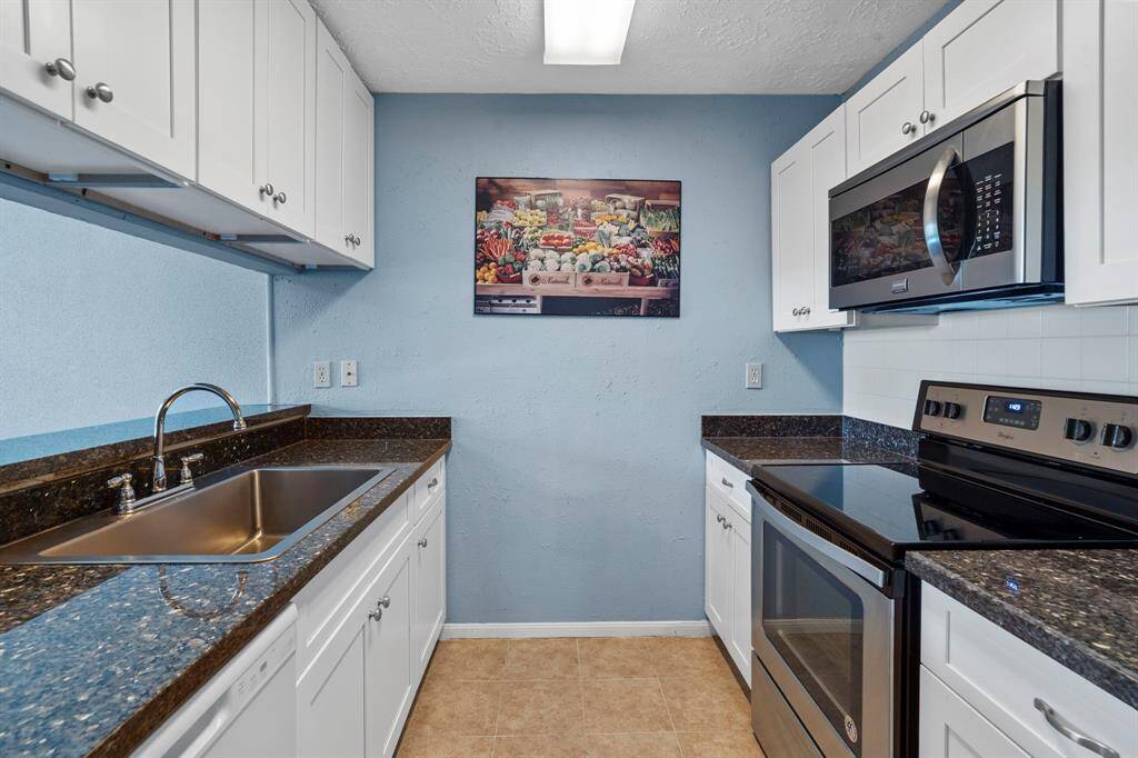 This charming galley-style kitchen offers a functional layout with sleek granite countertops, crisp white cabinetry, and stainless steel appliances. The double sink and overhead microwave maximize space and convenience. Ample storage and counter space make it easy to prep, cook, and entertain with ease.
