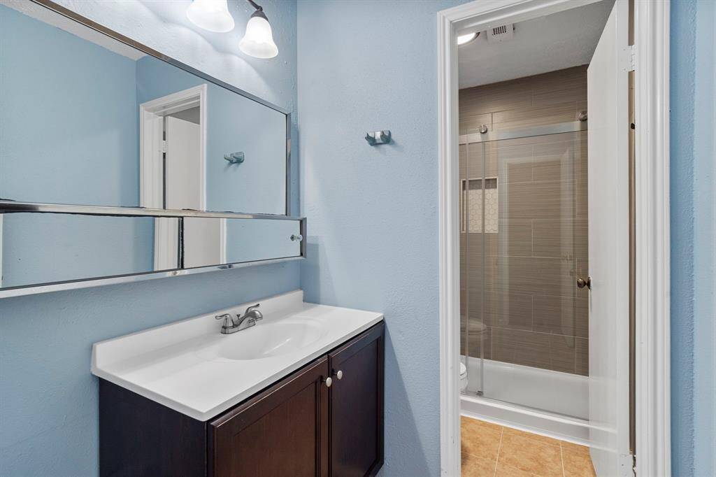 The primary bathroom offers tile flooring, sleek light countertops, a large mirror, and stylish dark fixtures and finishes, complete with a convenient newly renovated tile shower.