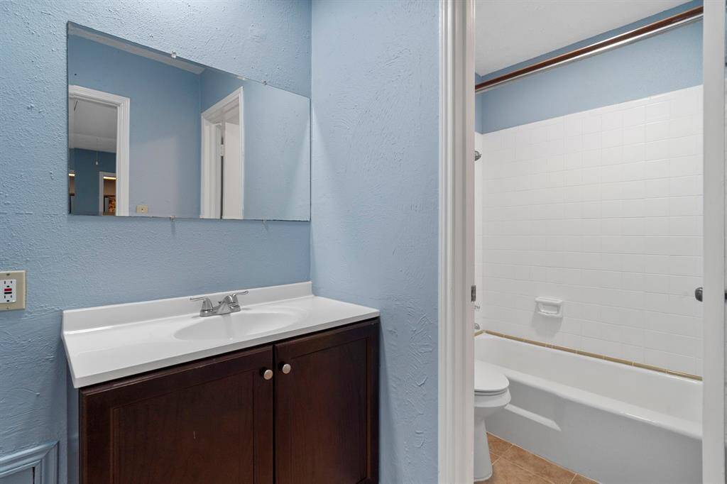 The secondary bathroom offers tile flooring, sleek light countertops, a large mirror, and stylish dark fixtures and finishes, complete with a convenient shower/tub combo.
