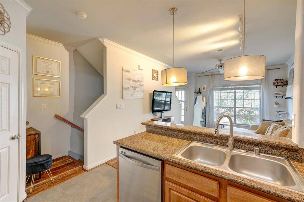 This cozy home features an open-concept layout with a modern kitchen overlooking the living area. It has granite countertops, stainless steel appliances, and ample natural light from large windows. The stairway leads to the upper level, adding a charming touch.