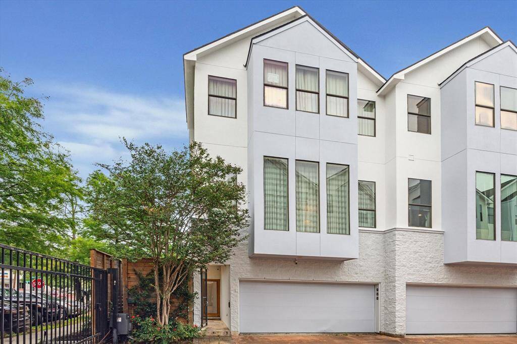 Modern three-story townhouse with a sleek facade, large windows, and a two-car garage. Situated in a gated community, it offers privacy and contemporary design, surrounded by greenery.
