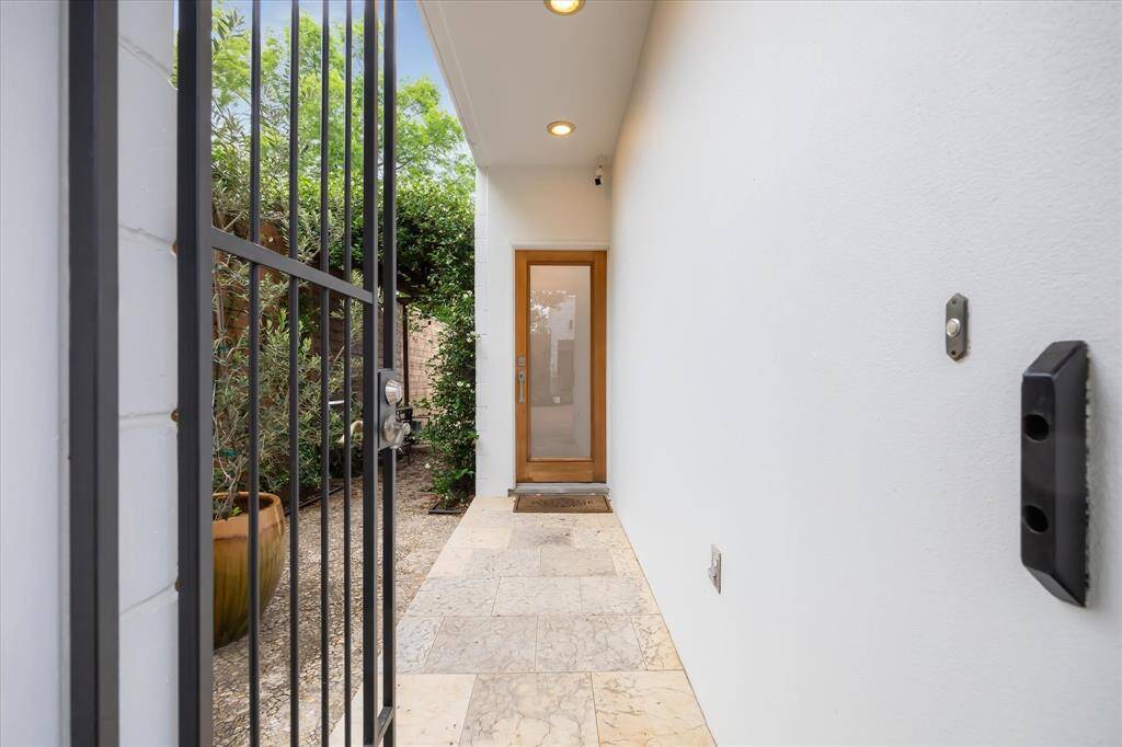 This photo shows a modern, inviting entryway with a wooden door, tiled flooring, lights, and a black metal gate.