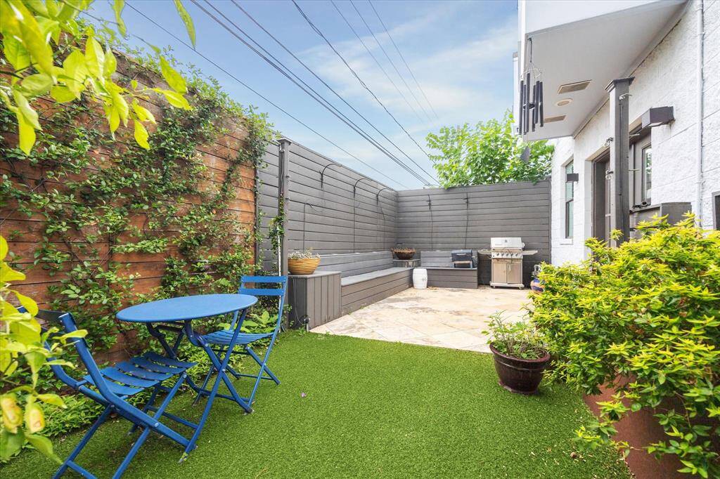 Cozy backyard with artificial grass, and a modern BBQ area. Surrounded by greenery and wood fencing for privacy, perfect for relaxing or entertaining outdoors.